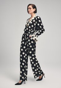Completo a pois bianco e nero con collo arruffato, pantaloni a gamba larga e maniche svasate, abbinato a tacchi a punta neri.