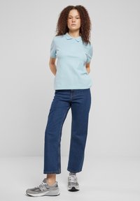 Šviesiai mėlynas polo marškinėliai trumpomis rankovėmis, derinami su tamsiai mėlynais tiesiais džinsais ir pilkais sportbačiais su baltais akcentais ir raišteliais.