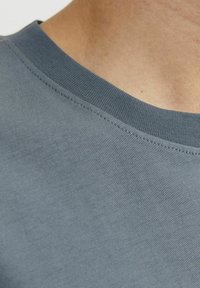 T-shirt à col rond en tissu doux et texturé. La couleur est bleu clair. Il présente un col côtelé et des coutures soignées le long des bords.