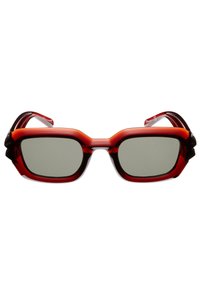 Lunettes de soleil rouges au design audacieux et angulaire. Les montures sont brillantes avec des verres teintés foncés et des accents texturés sur les côtés.