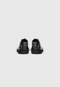 Schwarze Lederschuhe mit glatter Textur, runder Zehenpartie und niedriger schwarzer Gummisohle. Minimalistische Markierung an der Ferse. Rückansicht.