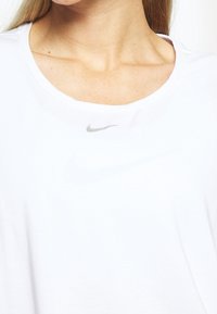 Camiseta deportiva de algodón blanco con escote redondeado, con un pequeño logo de Nike en gris en el pecho. Textura suave, corte relajado.