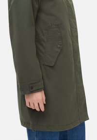 Olivengrøn parka med mat overflade, der har en sidelomme med klap, knaplukning ved ærmerne og lige kant. Casual fit, lavet af letvægtsstof.