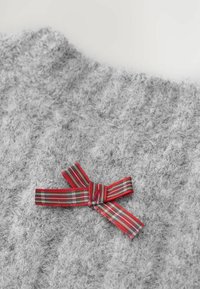 Grå, fuzzy sweaterdetalje med en rød ternet båndsløjfe. Stoffet ser tekstureret ud, og sløjfen har grønne og hvide accenter.