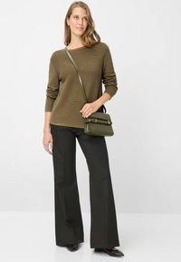 Olivgrüner, gerippter Pullover, schwarze weit geschnittene Hose und eine kleine grüne Umhängetasche mit goldenen Akzenten. Glatte Textur, minimalistisches Design.