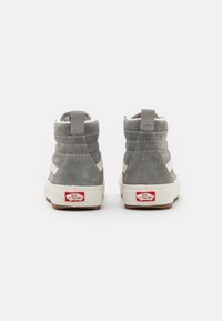 Zapatillas altas grises con parte superior de ante, franja blanca y suela de goma con dibujo marrón. Etiqueta de logo en el talón.
