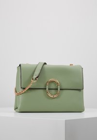 Borsa in pelle verde con una forma rettangolare semplice, accento in metallo circolare dorato e tracolla a catena rimovibile.