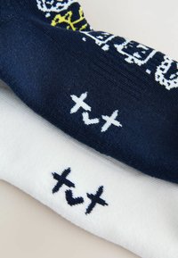 Bomuldssokker i marineblå og hvid. Den marineblå sok har et gult og hvidt grafisk design, mens den hvide sok har marineblå tekst og symbolsbroderi på manchetterne.