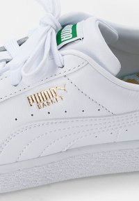 Białe skórzane trampki z teksturowaną białą gumową podeszwą, złotym logo "PUMA BASKET" oraz białymi sznurówkami. Posiada zieloną metkę z logo na języku.