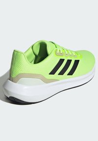 Scarpa sportiva verde con strisce nere, tomaia in rete, superficie texturizzata, intersuola bianca e suola in gomma nera. Presenta un colletto imbottito.