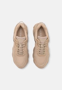 Beige athletic sneakers with mesh and suede materials, featuring rounded toe, laces, padded collar, and brand logo on the tongue.