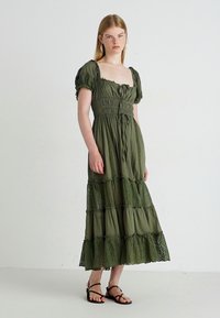 Olijfgroene, gelaagde maxi-jurk met poftmouwen. Bevat kantaccenten op de lagen en een strakke bodice met een strik in de taille.