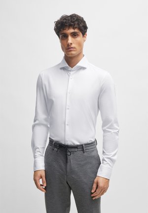White long-sleeve shirt with a spread collar and button closure, paired with gray textured trousers featuring an adjustable drawstring waist.