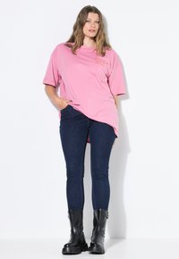 Camiseta rosa de gran tamaño con mangas cortas, que presenta un pequeño detalle bordado. Combinada con unos jeans skinny de mezclilla oscura y botas de tobillo negras.