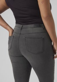 Gray skinny jeans made of denim, featuring back pockets and subtle stitching details. Worn with a black top, showing a smooth texture.