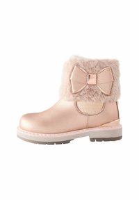 Botines metálicos cortos en rosa con puño de piel sintética y gran acento de lazo. Presentan un panel lateral texturizado y suela de goma para mayor tracción.