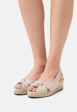 Beige espadrille wedges med en knyttet front, vævet jutesål og åben bagside, der viser tekstureret stof og et afslappet design.