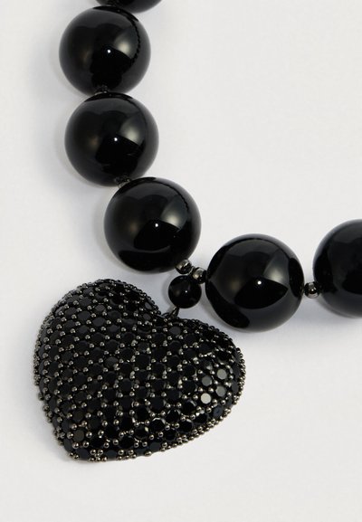 Melns krelles kaklarota ar lielām spīdīgām apaļām pērlēm un teksturētu sirds formas piekariņu, kas rotāts ar mazām melnām akmentiņām.