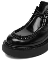 Sandalii mocasini din piele neagră lucioasă, cu talpă groasă neagră, cusături detaliate și șireturi negre, pe un fundal alb.