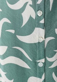 Zelena i bijela košulja s uzorkom valovitih dizajna, zatvaranje na kopče s okruglim, svijetlim gumbima i mekanom teksturom tkanine.