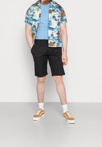 Short-sleeve, multicolored Hawaiian shirt with a tropical print, paired with black shorts and beige sneakers, worn with white socks.
