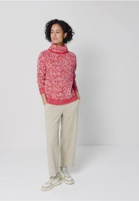 Röd och vit prickig polotröja, avslappnad passform, parat med ljusbeige vida byxor och krämfärgade sneakers med gröna detaljer.