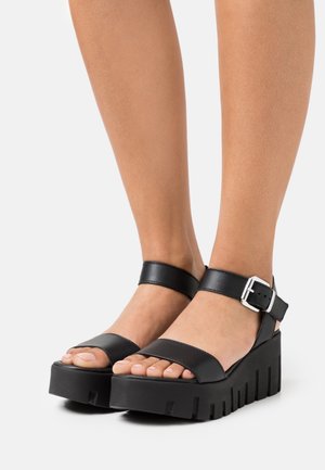 Sandales à plateforme noires avec larges brides, boucle réglable à la cheville, semelle texturée et design à bout ouvert.