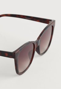 Ochelari de soare cu model țestoasă, cu ramă mare în formă de ochi de pisică, lentile maronii cu gradient, material din plastic neted și accente argintii pe balamale.