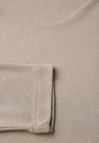 Beige kangas, jolla on sileä pinta, jonka hiha on taitettu ja näkyviä ompeleita, suunniteltu rentoon, arkiseen tyyliin.