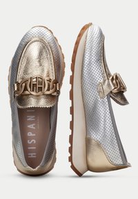 Scarpe in pelle argentata metallica con accenti dorati, caratterizzate da un design perforato, un ornamento a catena e suola in gomma testurizzata.