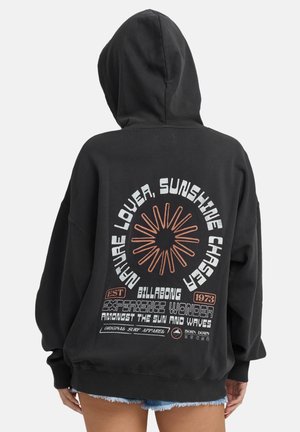 Zwarte hoodie met een grote graphic op de achterkant met oranje en witte tekst, zonnestraalontwerp en een oversized pasvorm met een voorkantzak.