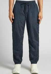 Marinblå lätta cargo byxor med elastisk midja och dragsko, med en krinklad textur och sidofickor. Bärs med vita sneakers.