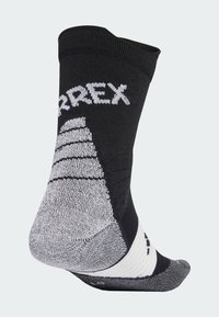 Μαύρη και γκρι αθλητική κάλτσα με υφές, ενισχυμένη υποστήριξη στον αστράγαλο, και το λογότυπο "Terrex" υφασμένο σε λευκό στο επάνω μέρος.