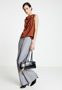 Top marrone drappeggiato, pantaloni grigi a gamba larga con dettagli a bottoni, borsa nera con catena e tacchi appuntiti. Tessuto dalla texture liscia.