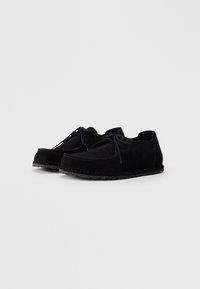 Schwarze Wildleder-Schnürschuhe für den Alltag mit dicken, genähten Sohlen, auf einem schlichten hellgrauen Hintergrund präsentiert.