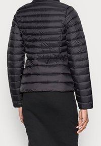 Svart puffjacka med en figurnära silhuett, vertikalt sydd mönster och långa ärmar, tillverkad av slät, lättviktig tyg.