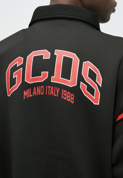 Must läikiv must polo-särk, millel on suur ja julge punane "GCDS" logo ning selle all "MILANO ITALY 1988". Särgil on sile tekstuur ja peened kangadetailid.