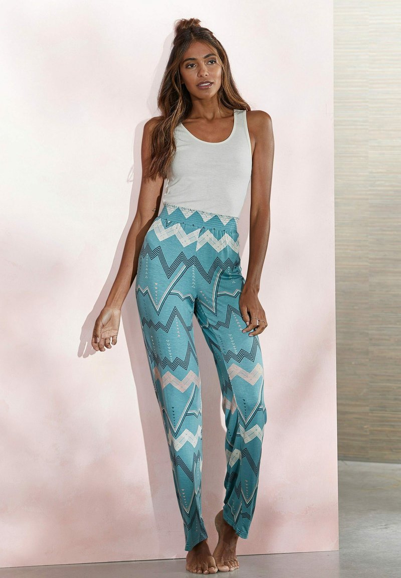 Turquoise patterned pants with zigzag designs in white and pink, paired with a fitted white tank top. The fabric appears lightweight.