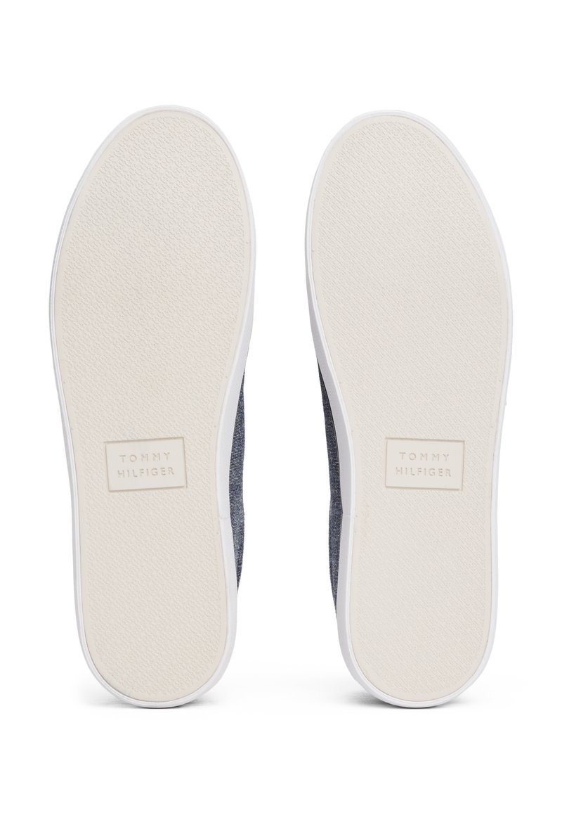 Chaussures slip-on à upper en tissu bleu avec une semelle en caoutchouc blanc, présentant un motif de grip texturé et un petit logo de la marque sur la semelle.