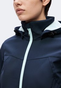 Personne portant une veste bleu marine avec une fermeture éclair bleu clair et un col montant, montrée du cou au haut du torse.
