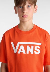 Oranžové bavlněné tričko s velkým bílým logem "VANS" na hrudi, kulatým výstřihem a krátkými rukávy. Hladký povrch, volný střih.