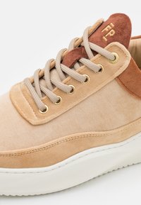 Baskets en suède beige avec de épaisses lacets beiges, œillets dorés, languette et col de couleur rouille, semelle en caoutchouc blanche, et "FP" brodé sur la languette.