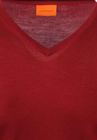 Roter V-Ausschnitt-Pullover aus feinem Strickstoff. Verfügt über eine glatte Textur und ein orangefarbenes Etikett mit der Aufschrift "SUITABLE".