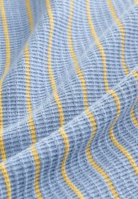 Kootud helesinine kangas tekstuursete triipudega; vahelduvad kollased jooned loovad materjalil lainelise mustri.