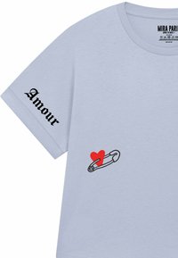 T-shirt bleu clair à manches courtes avec "Amour" en noir sur la manche et un cœur rouge à côté d'un graphique de épingle de sûreté noire sur le devant.