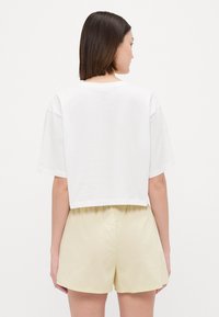 Kortgeknipte witte t-shirt met korte mouwen, gecombineerd met lichtgele shorts. De stof is zacht en glad, met een elastische tailleband op de shorts.