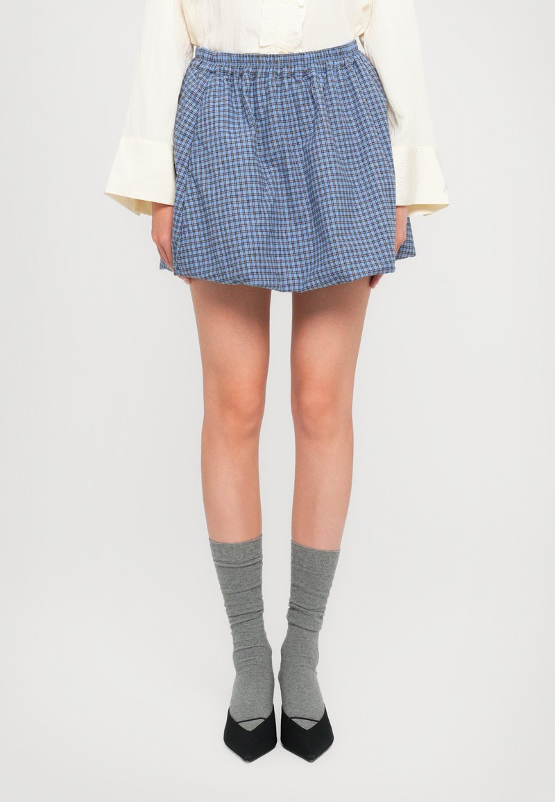 Falda a cuadros azul y blanca con una cinturilla elástica, diseño en capas, combinada con calcetas gris hasta la rodilla y zapatos negros de punta.