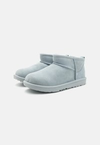 Botas de tobillo de ante azul claro con punta redondeada, detalles de costura y suela de goma texturizada. Diseño minimalista con un puño doblado.