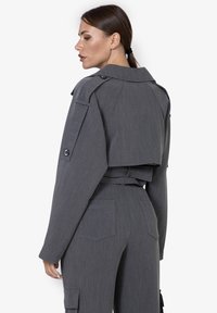 Grijze cropped jack met een gestructureerde kraag, militaire knopen en bijpassende hooggetailleerde broeken met opgestikte zakken en een subtiele textuur.