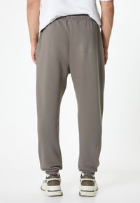 Pantalones de chándal grises con cintura elástica, puños ajustados y bolsillos laterales. El material parece suave y cómodo. Llevados con zapatillas.